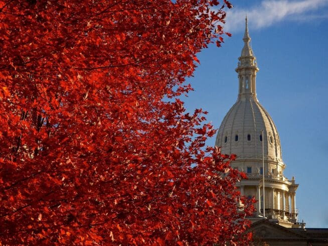Michigan Capitol dome in Autumn with a tree with red leaves in the foreground..